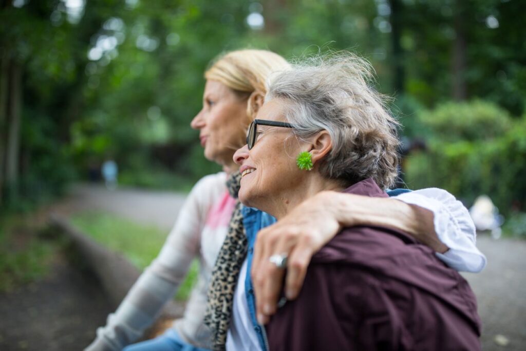Zwei Frauen sitzen gemeinsam im Freien und blicken ruhig in die Ferne.