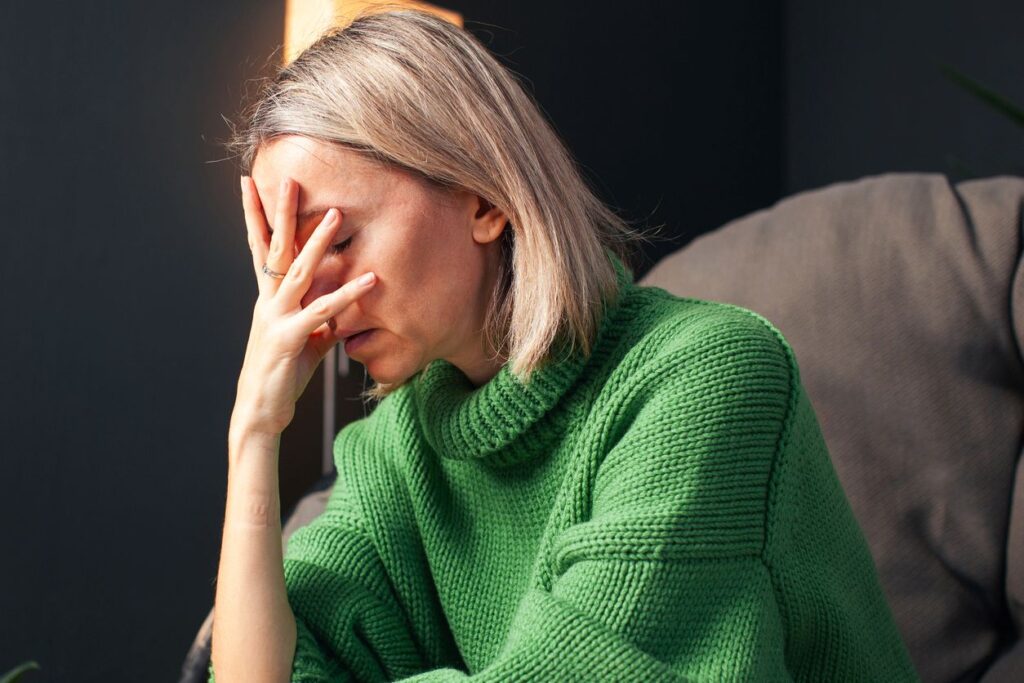 Eine nachdenkliche Frau sitzt mit der Hand vor dem Gesicht und wirkt emotional belastet.