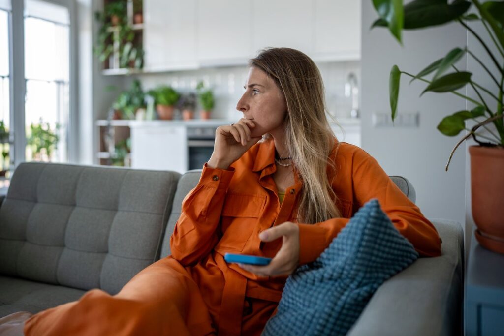 Eine nachdenkliche Frau sitzt auf einem Sofa und blickt zur Seite.