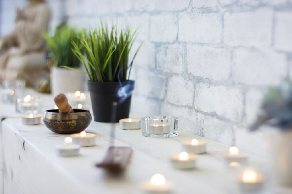 Eine ruhige Ecke mit brennenden Teelichtern, einer Klangschale, Räucherwerk und grünen Pflanzen lädt zu Stille und Meditation ein.