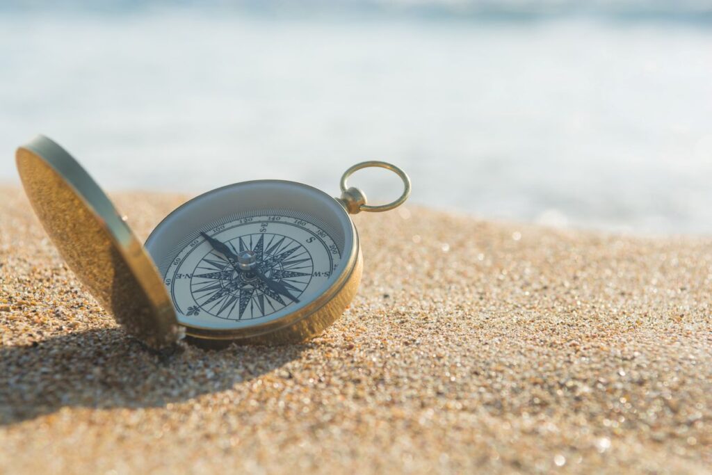 Ein geöffneter Kompass liegt im warmen Sonnenlicht auf einem Sandstrand und symbolisiert Orientierung und den eigenen Weg.