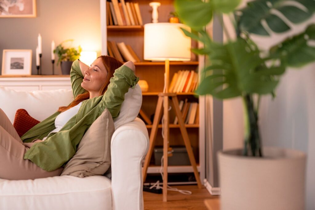 Frau entspannt auf einem Sofa in einem warm beleuchteten Wohnraum